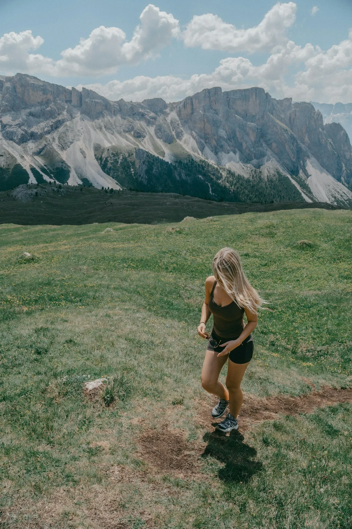 A woman hiking up a grassy mountain path with jagged peaks behind her